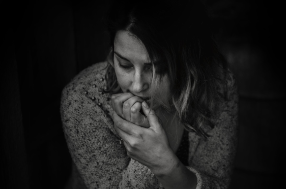 A sad woman bites her nails while looking downwards at the floor. The picture is black and white